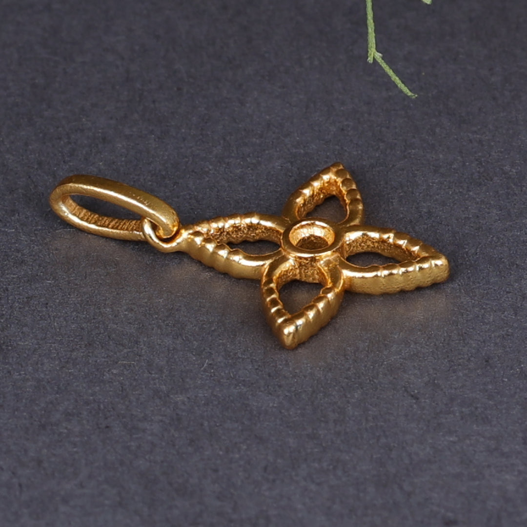 Close-up of a textured gold-plated four-petal flower pendant charm with a central round opening